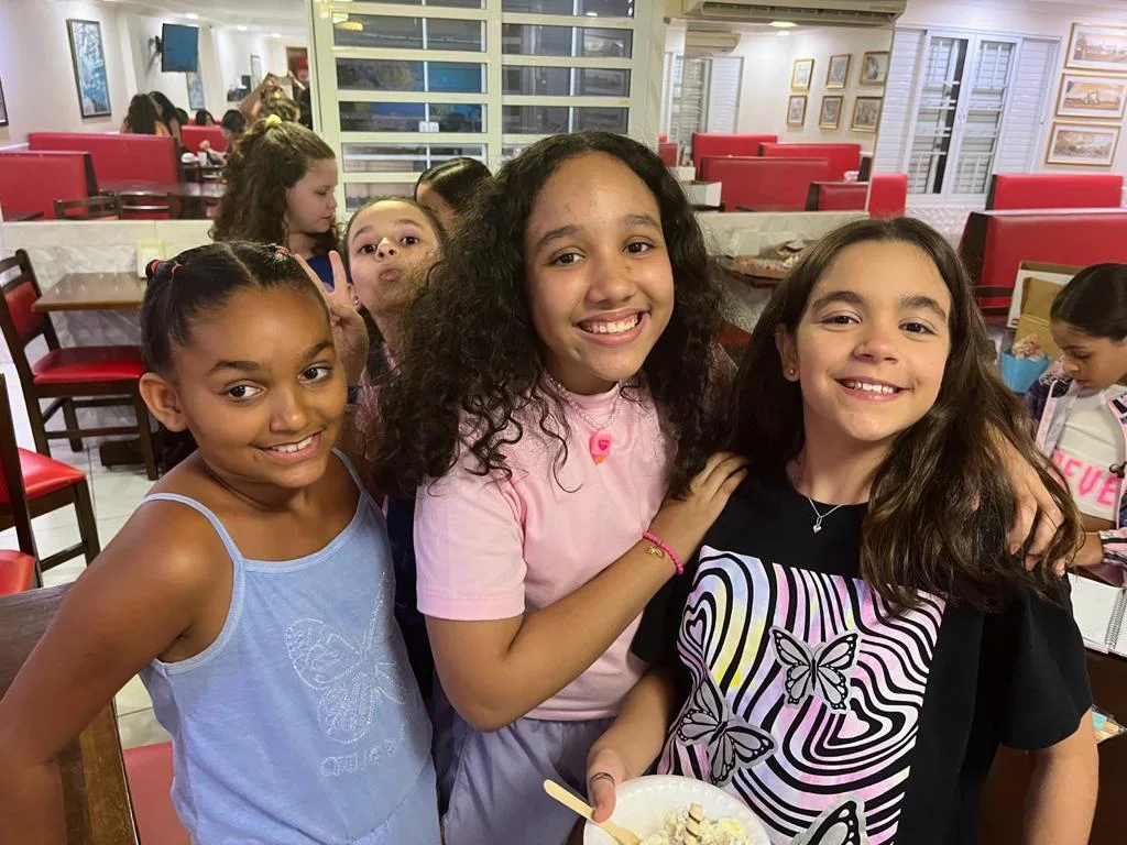 Três amigas sorrindo, com o salão ao fundo