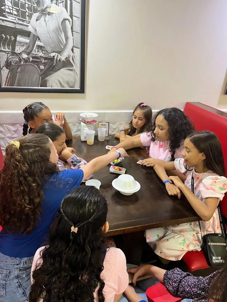 Crianças jogando à mesa, com os sofás vermelhos do salão