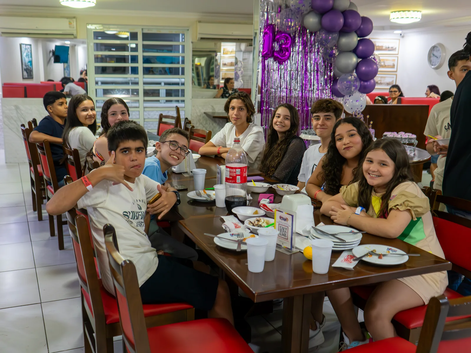 Turma reunida à mesa no salão, com a decoração roxo e prata ao fundo