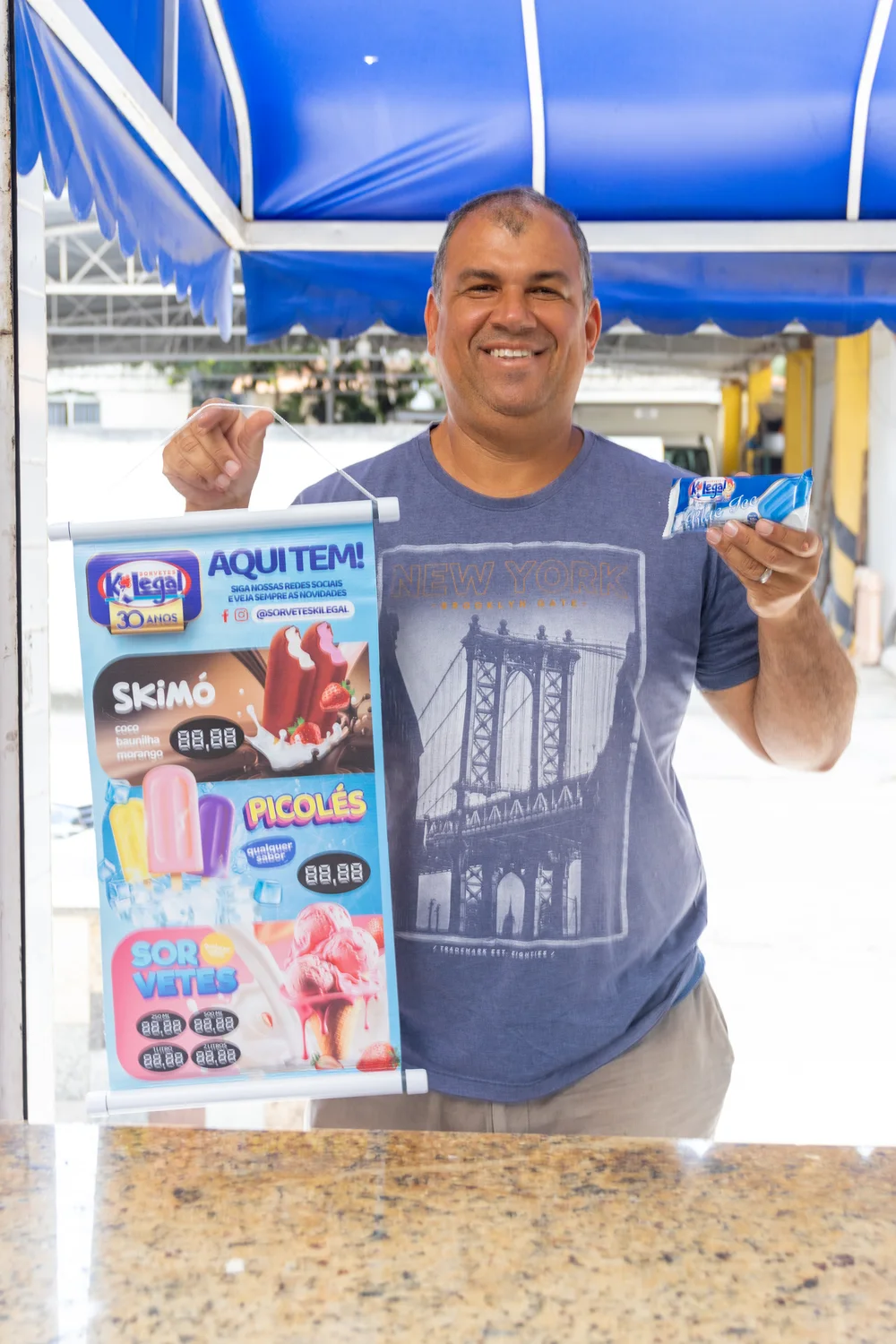 Revendedor sorrindo com o banner Aqui tem! KiLegal e um picolé na mão